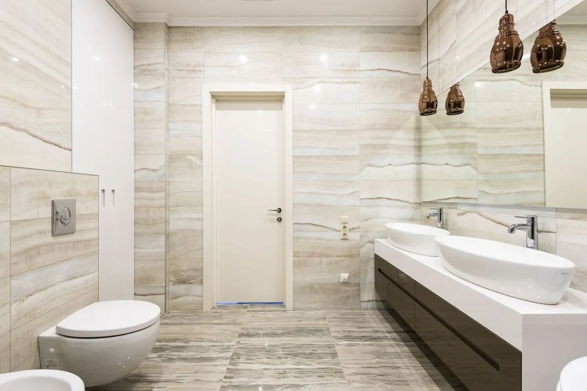 Beige bathroom with double sinks, vanity counter, and toilet in a clean modern interior