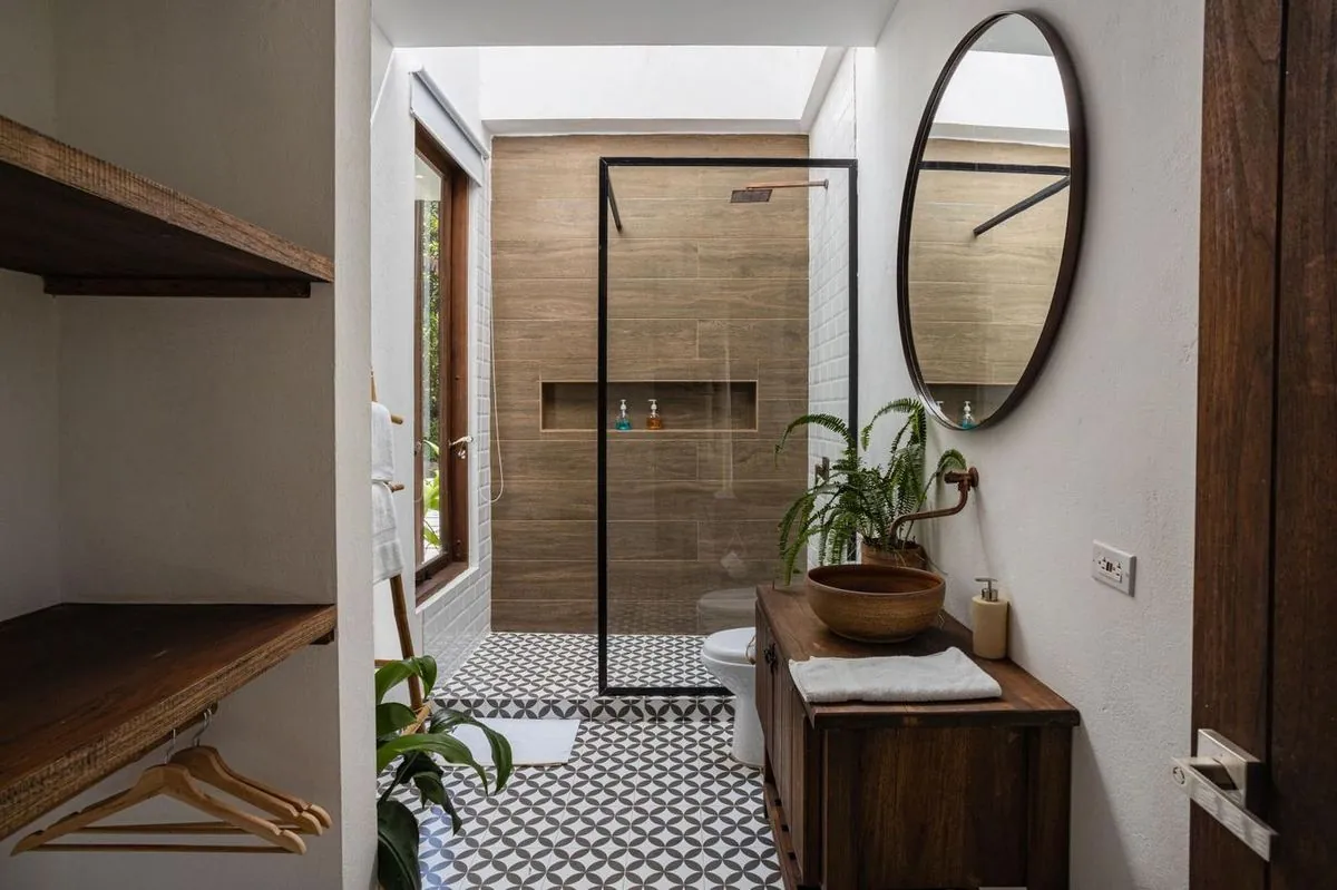 Modern bathroom with a glass walk-in shower, wood-look tile wall, vessel-sink vanity, and round mirror