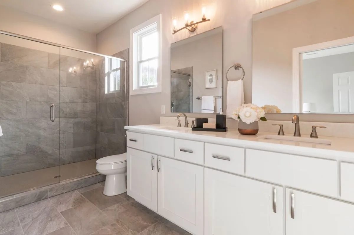 Bright contemporary bathroom with a glass shower, vanity, and white cabinets.