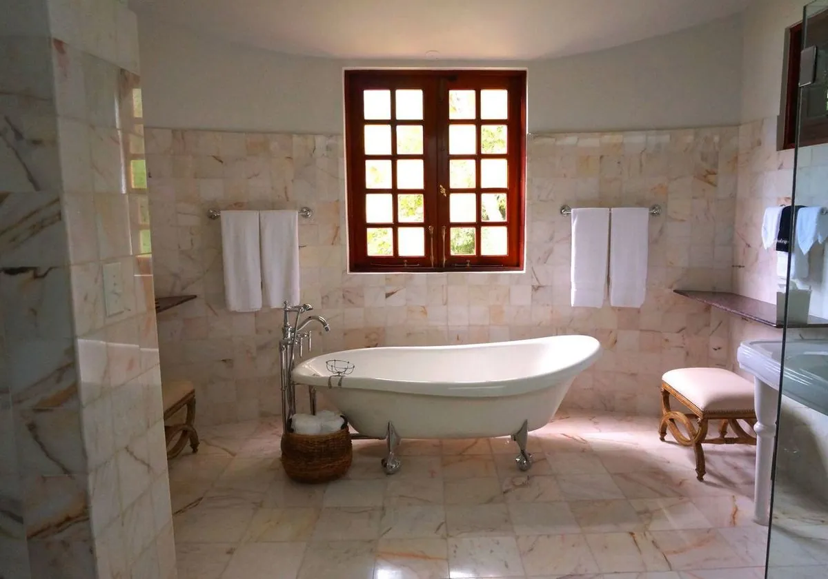 Classic freestanding bathtub with marble tiles and a framed glass window.