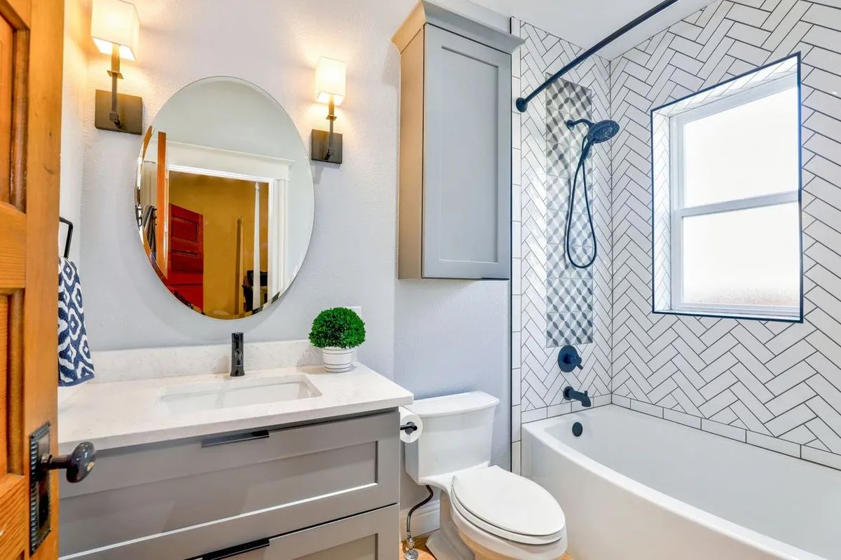 Modern bathroom with chevron tiles, an oval mirror, and sleek fixtures.