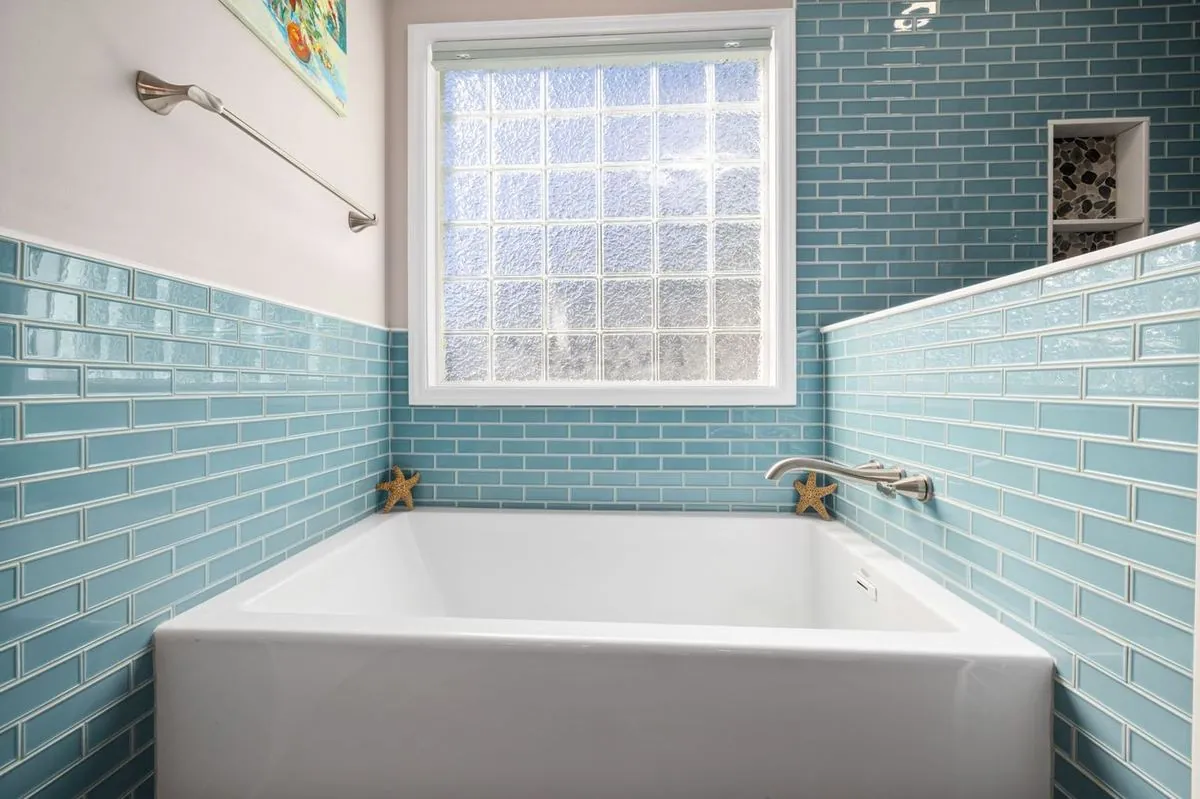 White bathtub against a bright turquoise tiled bathroom wall.