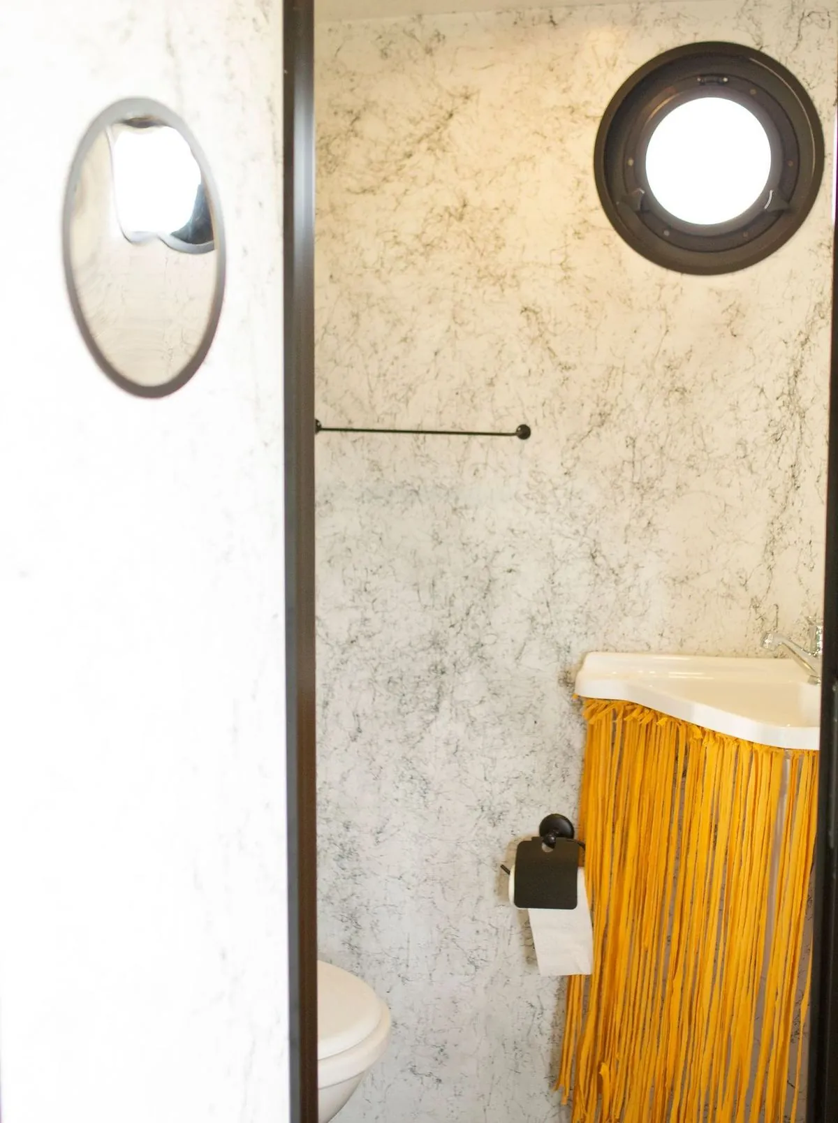 Stylish small bathroom with a marble wall, round window, and modern sink.