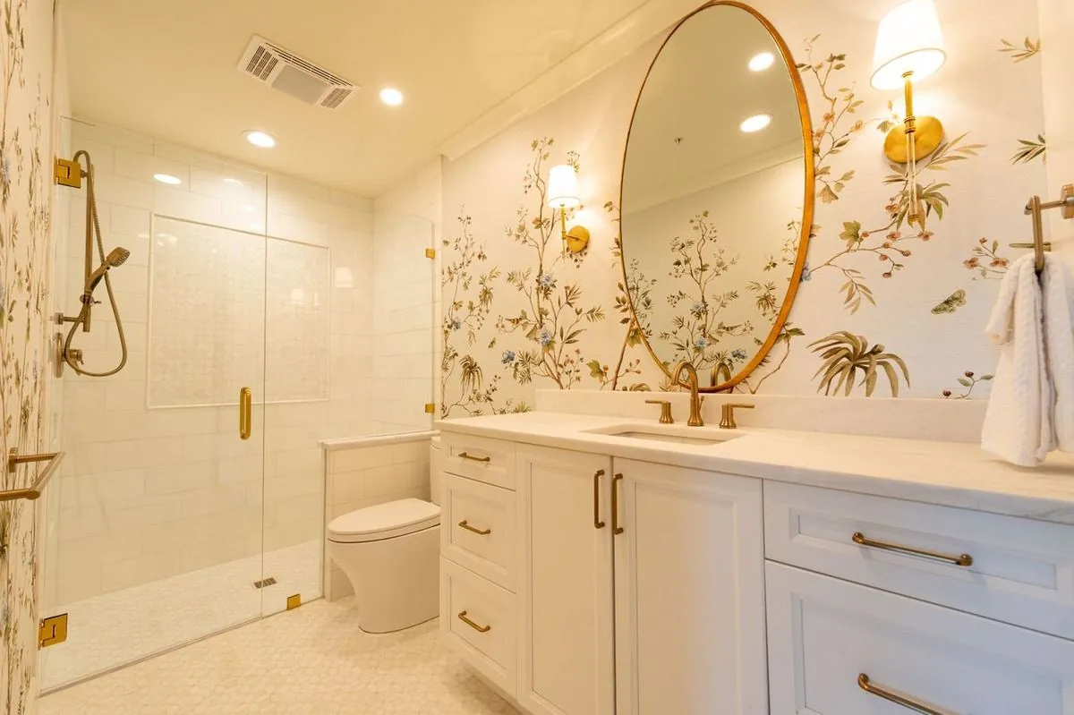 Modern bathroom with elegant floral wallpaper, gold fixtures, and a large round mirror