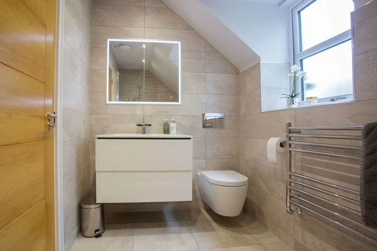 Stylish bathroom with wall-mounted toilet, sink, and illuminated mirror