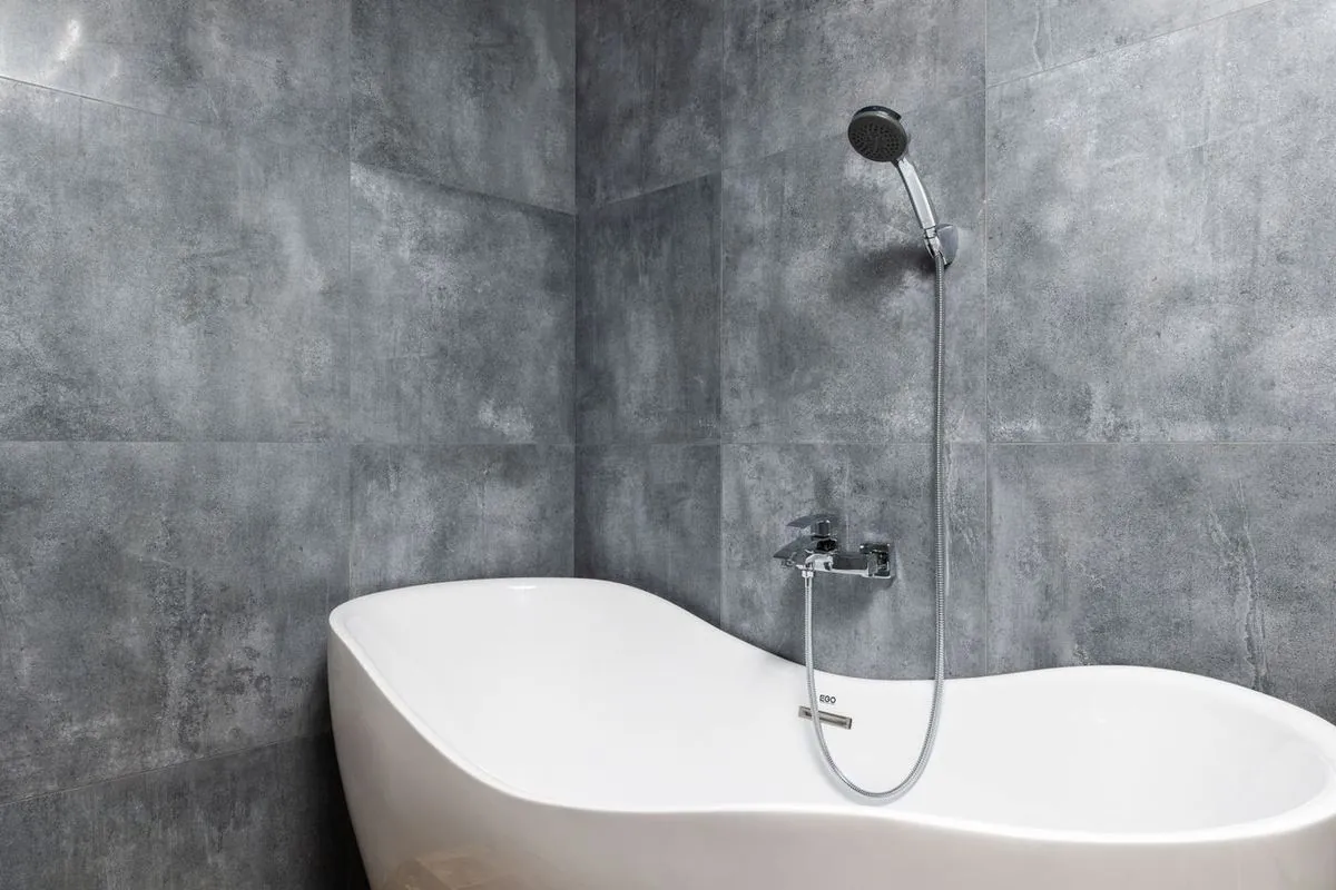 White freestanding tub against gray tile wall with handheld shower.