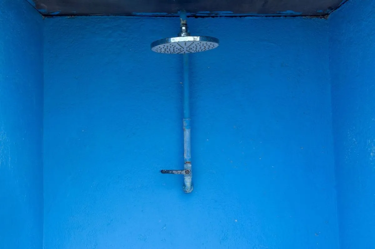 Blue textured shower area with single metal rain shower head against a vibrant wall.