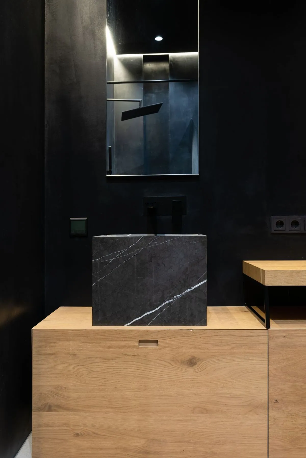 Moody bathroom detail with a black marble vessel sink on a wood vanity beneath a tall mirror.