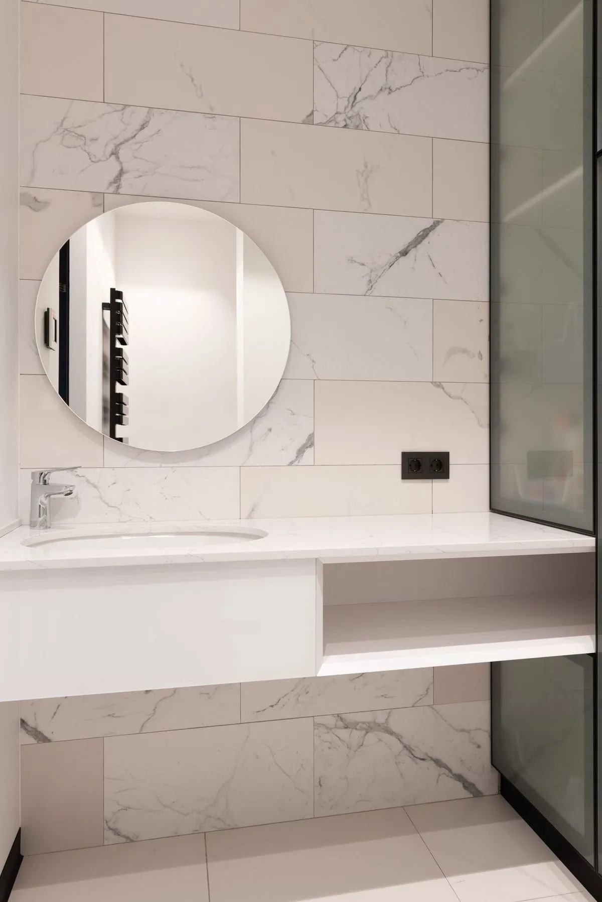 Marble-tiled bathroom with a round mirror over a navy floating vanity.