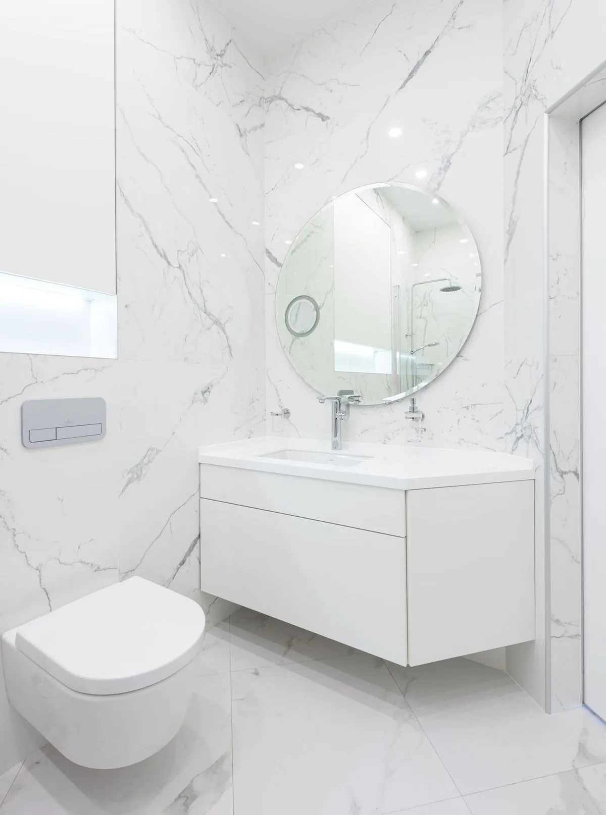 A sleek, minimal bathroom with white marble walls and round mirror.