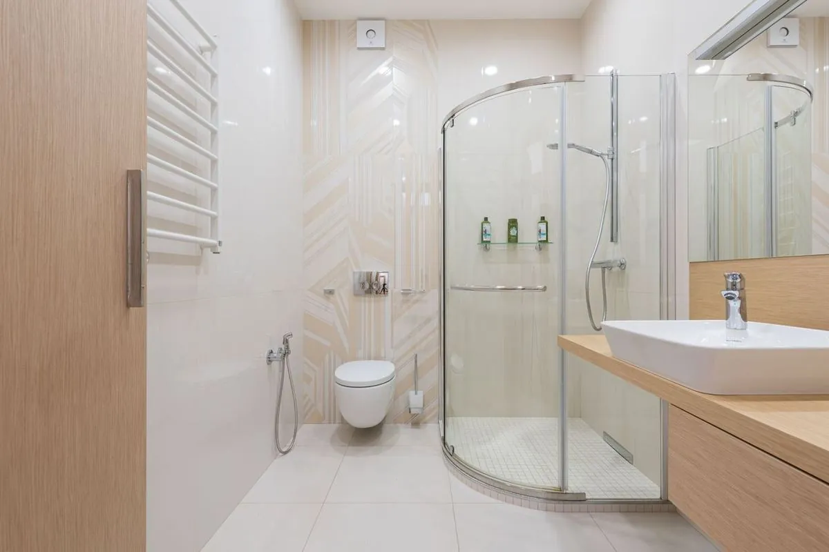 Shower cabin with transparent glass doors in a modern bathroom with wooden furniture and tiled walls.