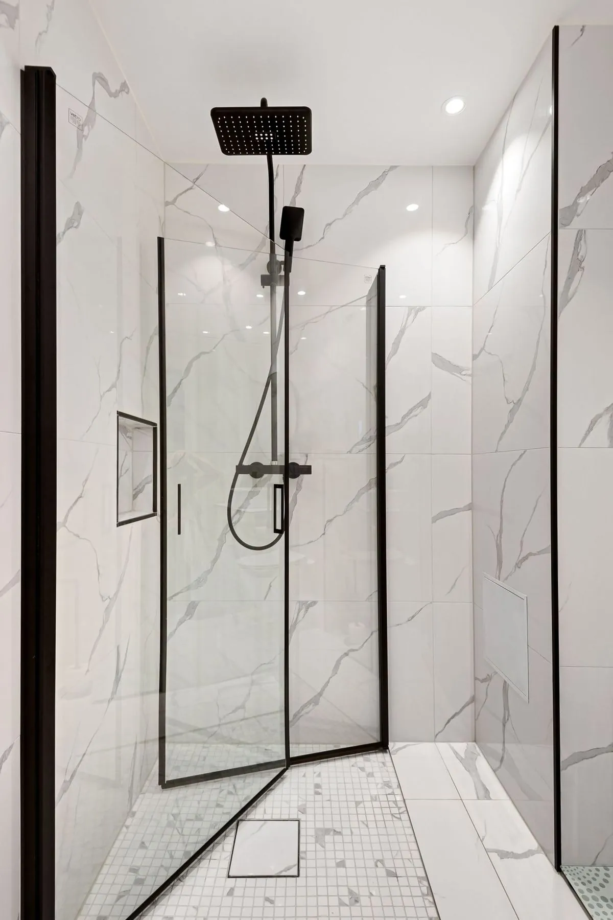 Walk-in shower with black fixtures, marble-look walls, and mosaic tile floor