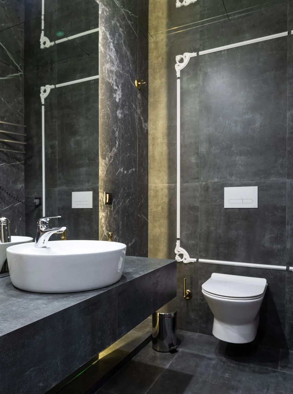 Dark marble bathroom with a vessel sink, wall-hung toilet, and gold accents