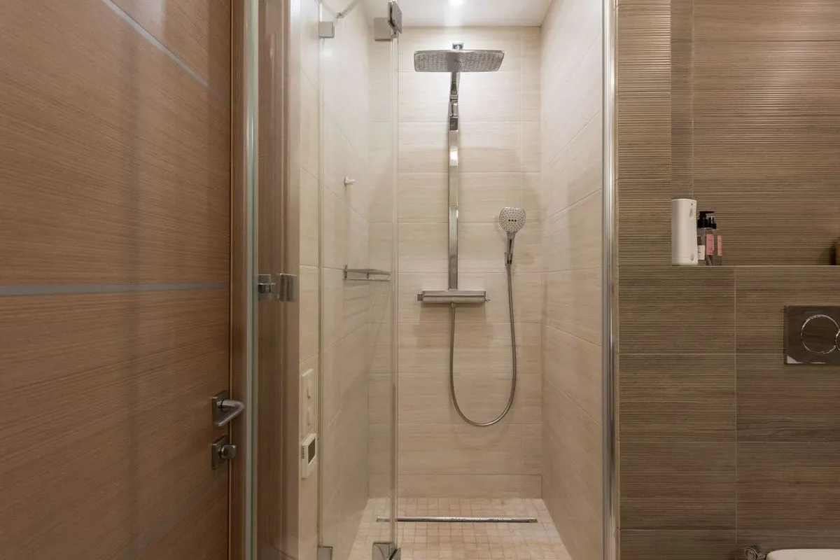 Beige-tiled walk-in shower with rainfall showerhead and glass door.