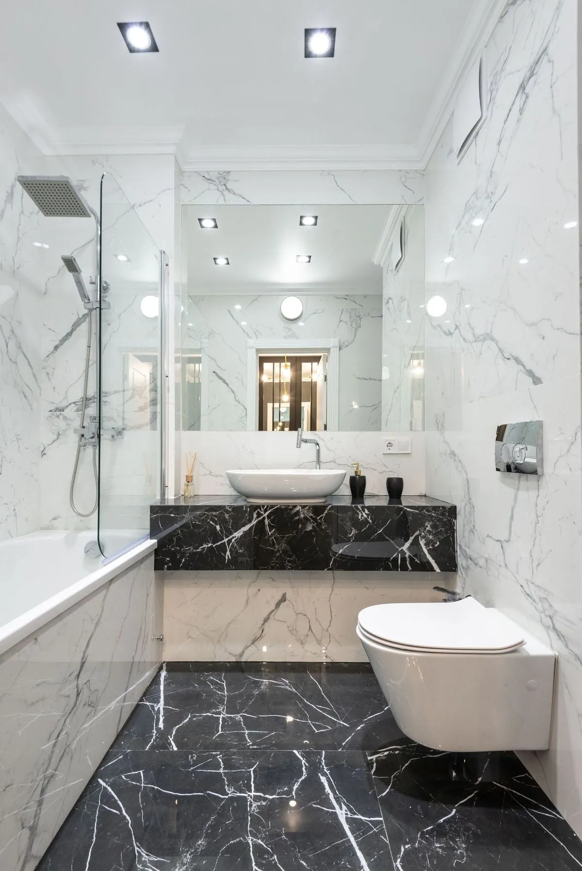 Marble bathroom with glass shower, floating black vanity counter and vessel sink.
