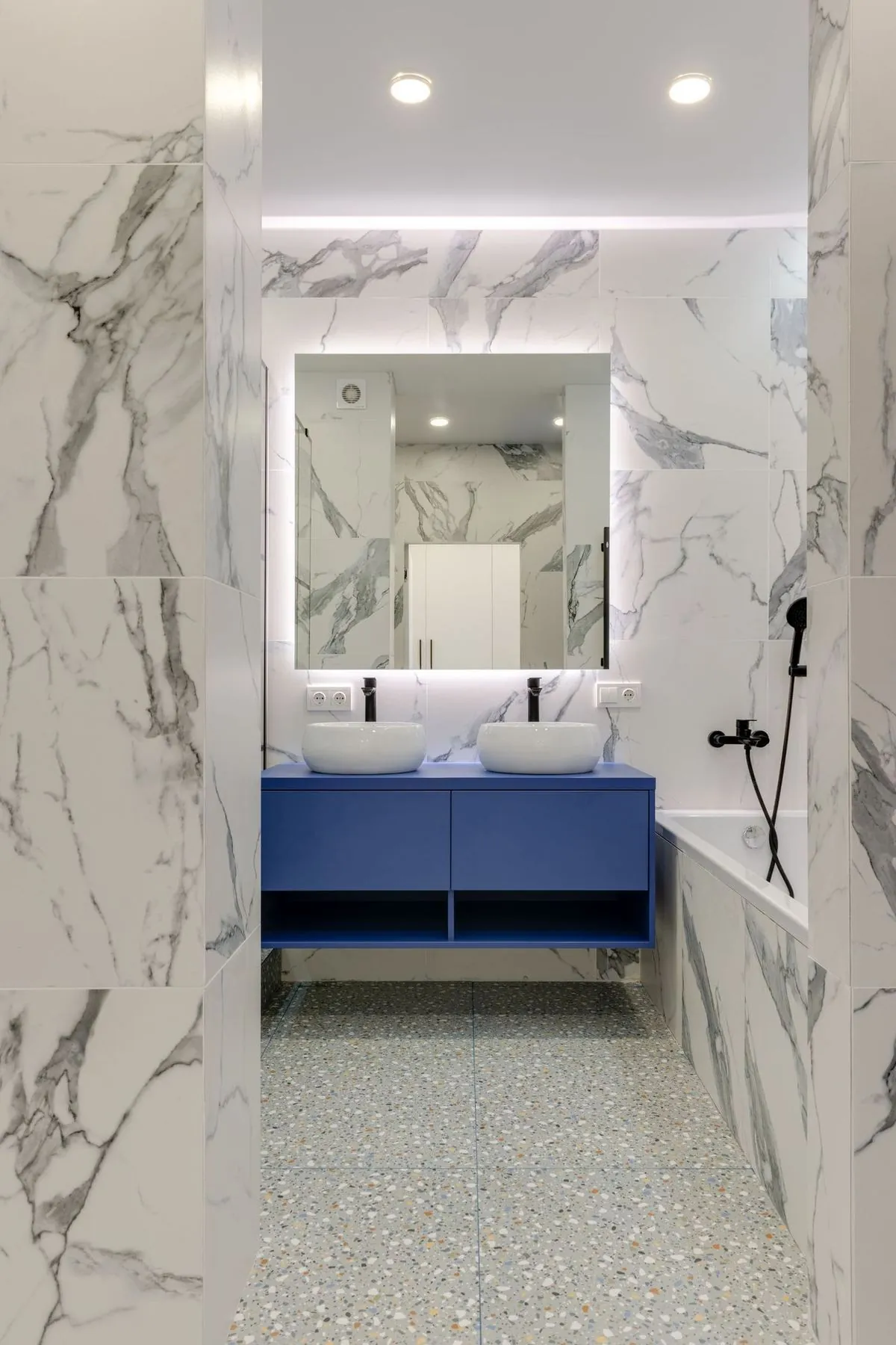 Double sinks on a blue vanity cabinet with marble walls