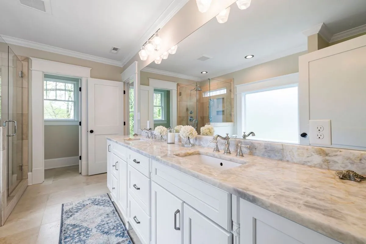 Spacious bathroom with marble countertop, glass shower, and elegant lighting