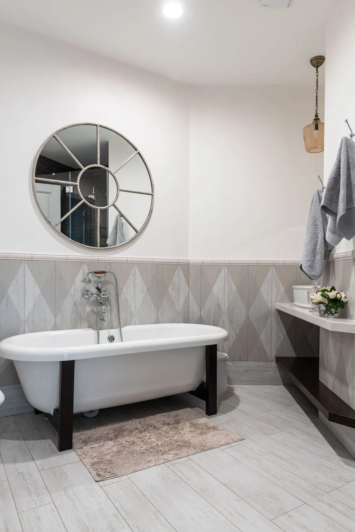 Freestanding white bathtub under a round mirror in a stylish modern bathroom