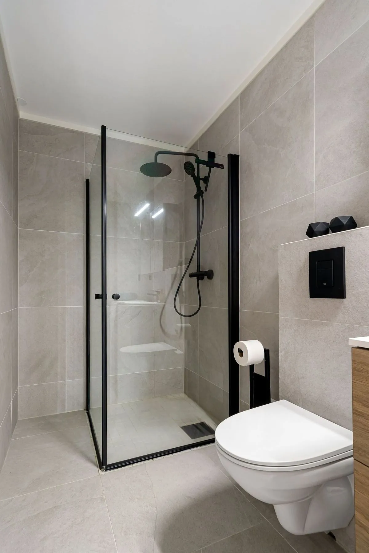 Modern bathroom with frameless glass shower, gray tiles and compact design.