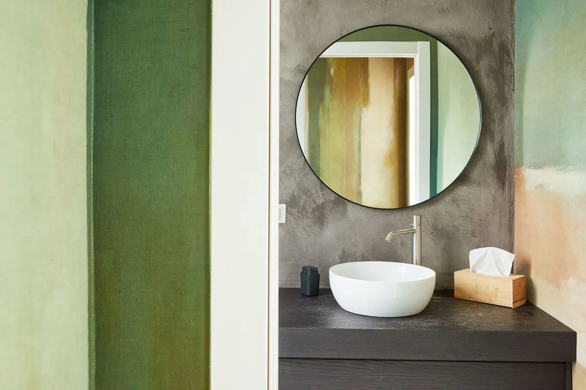 Powder room with a sink, round mirror and green walls in a modern bathroom.