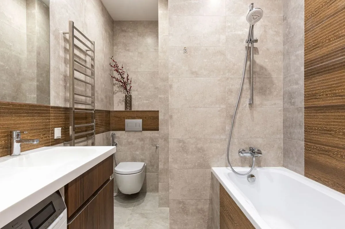Compact modern bathroom with a white bathtub, shower fixture and wood vanity.