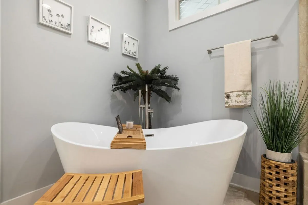 Freestanding soaking tub with a bamboo bath tray, wooden stool and potted plants in a spa-styled bathroom.